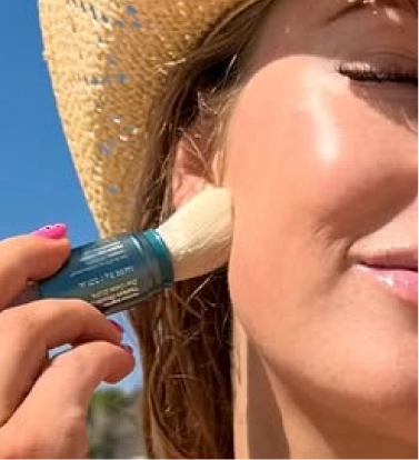 Mujer joven aplicándose protección solar en polvo para prevenir manchas en la piel durante el verano